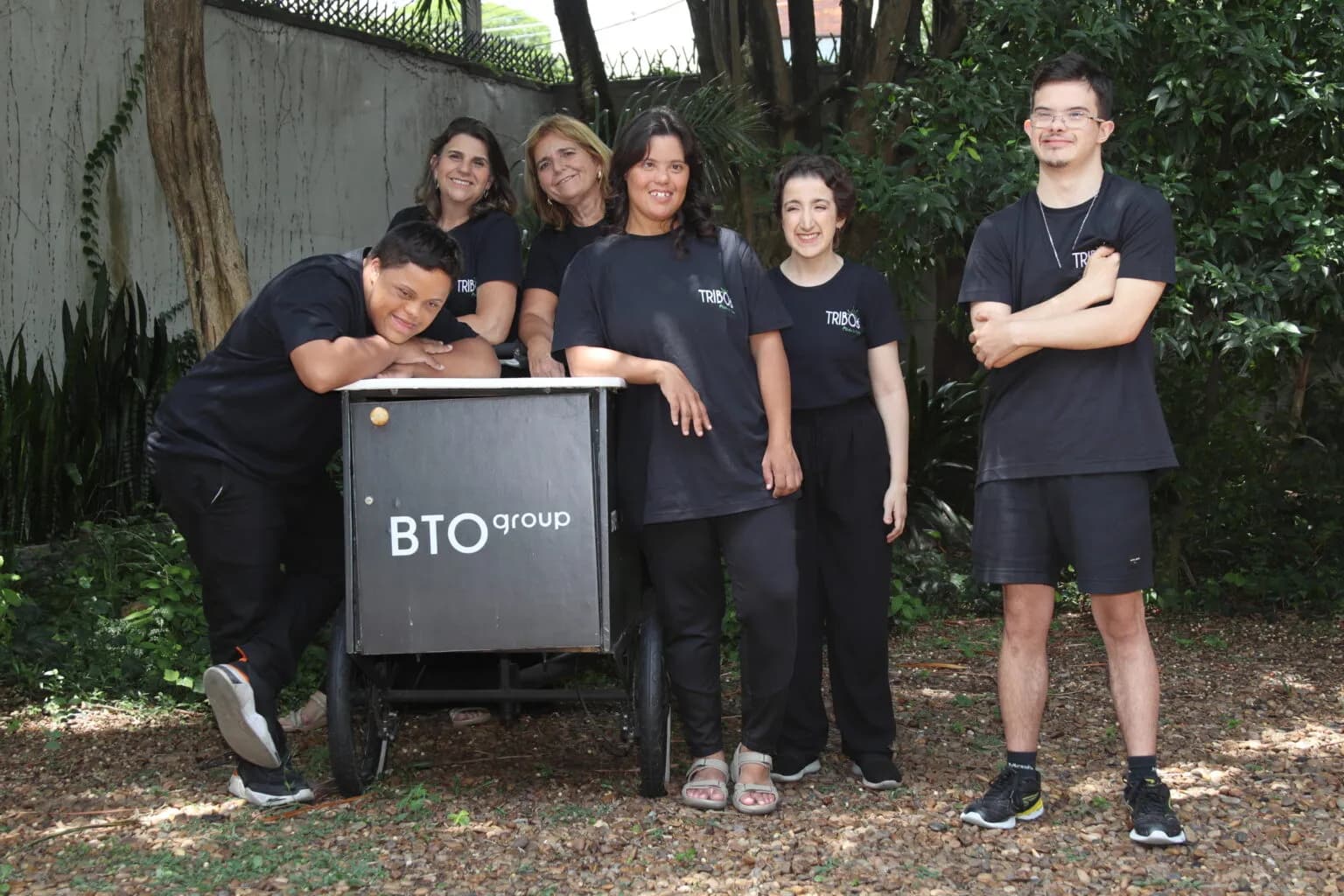 Integrantes do programa TRIBO da BTO+ reunidos ao redor de uma bike de carga BTO group em um jardim arborizado